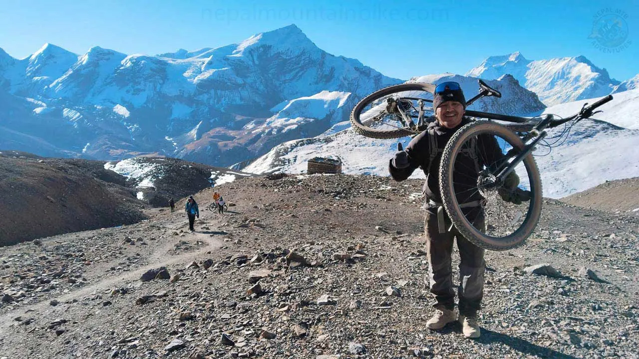 Cyclist carrying mountain bike up to Thorong-La pass, the highest point on the Annapurna Circuit at an altitude of 5416m during the Nepal MTB expedition in the Himalayas.