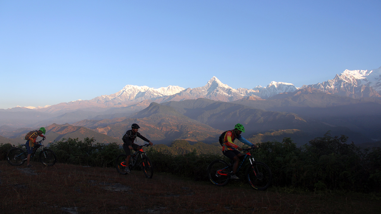 Three mountain bikers are enjoying their ride with the view of Dhaulagiri, Annapurna I, Fishtail and Annapurna III starting from left.